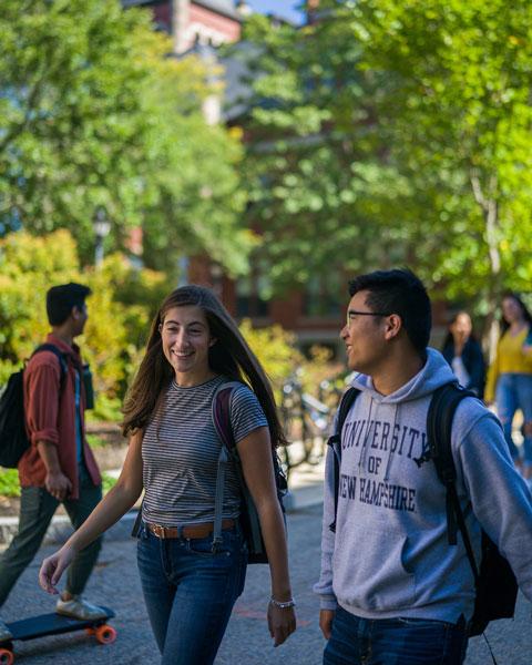 Students walk and skateboard in front of T-Hall at UNH.